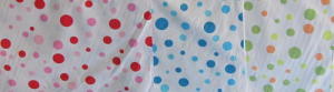 Three rolls of fabric on roll with spots of different sizes in shades of blue, another in shades of red and the third in orange and green