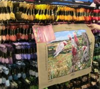 Tapestry of a Flock of Pink and White Cockatoos being held up against a rack of Tapestry Threads